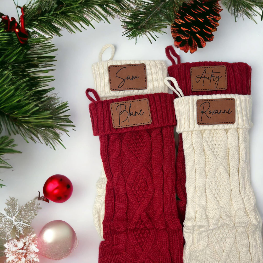 Two Christmas stockings with personalized name tags on a festive background with ornaments and greenery.