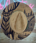 Cowboy hat with deer and cabin design on a wooden surface