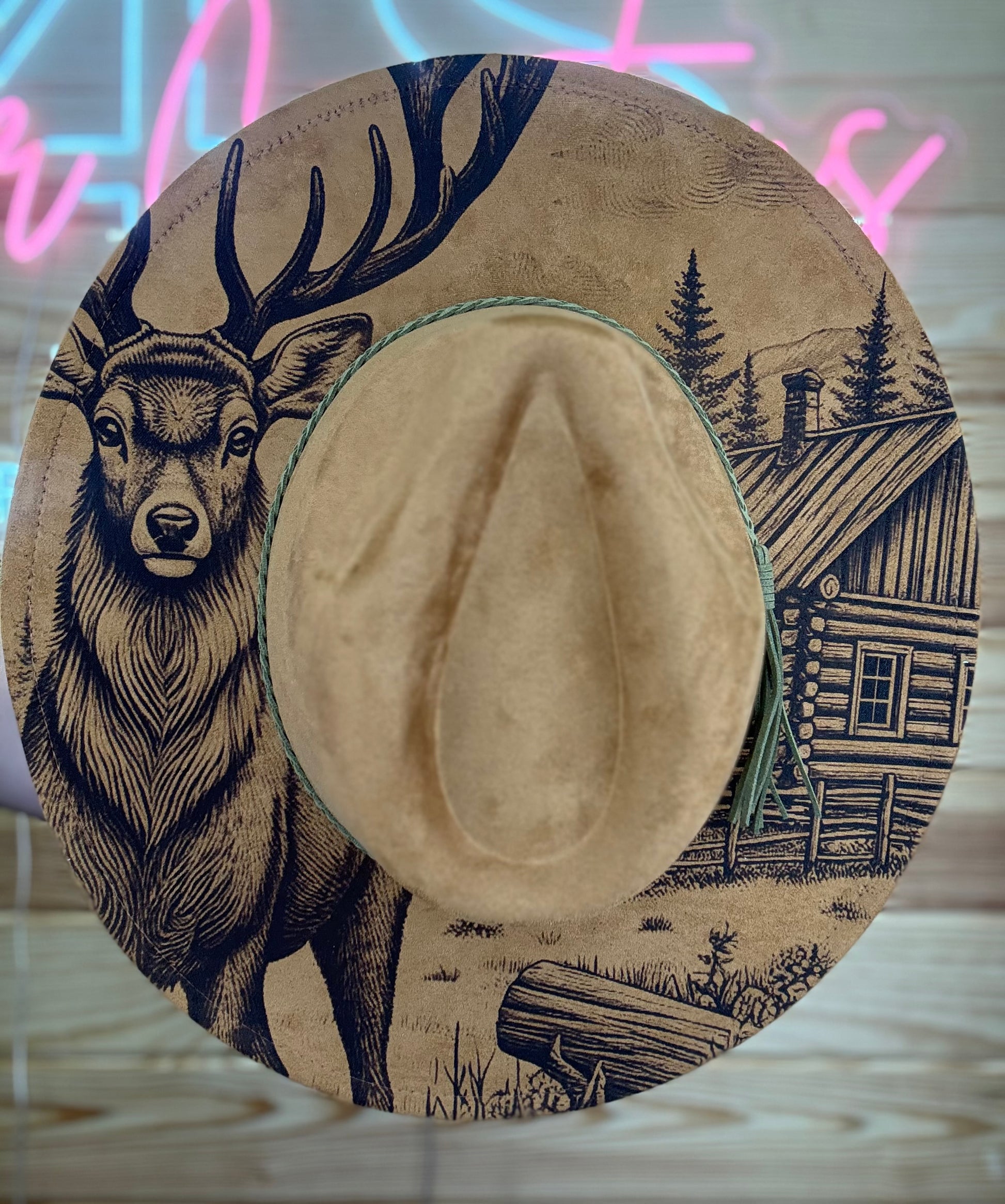Cowboy hat with deer and cabin design on a wooden surface