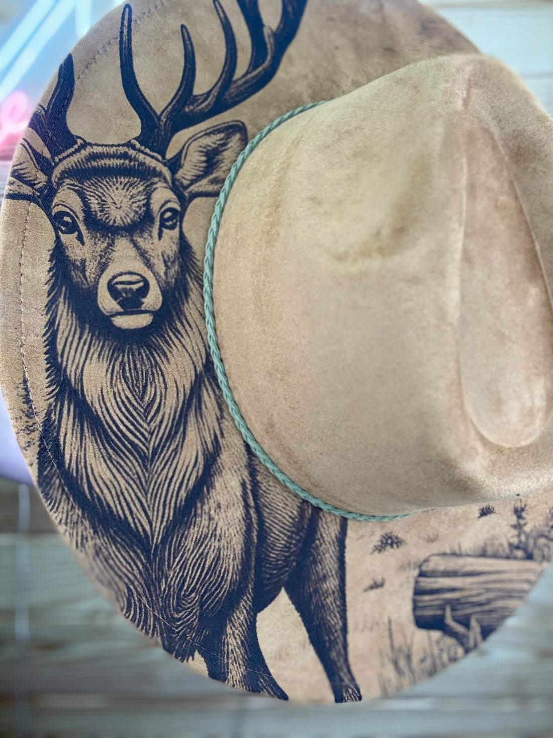 Cowboy hat with deer and cabin design on a wooden surface