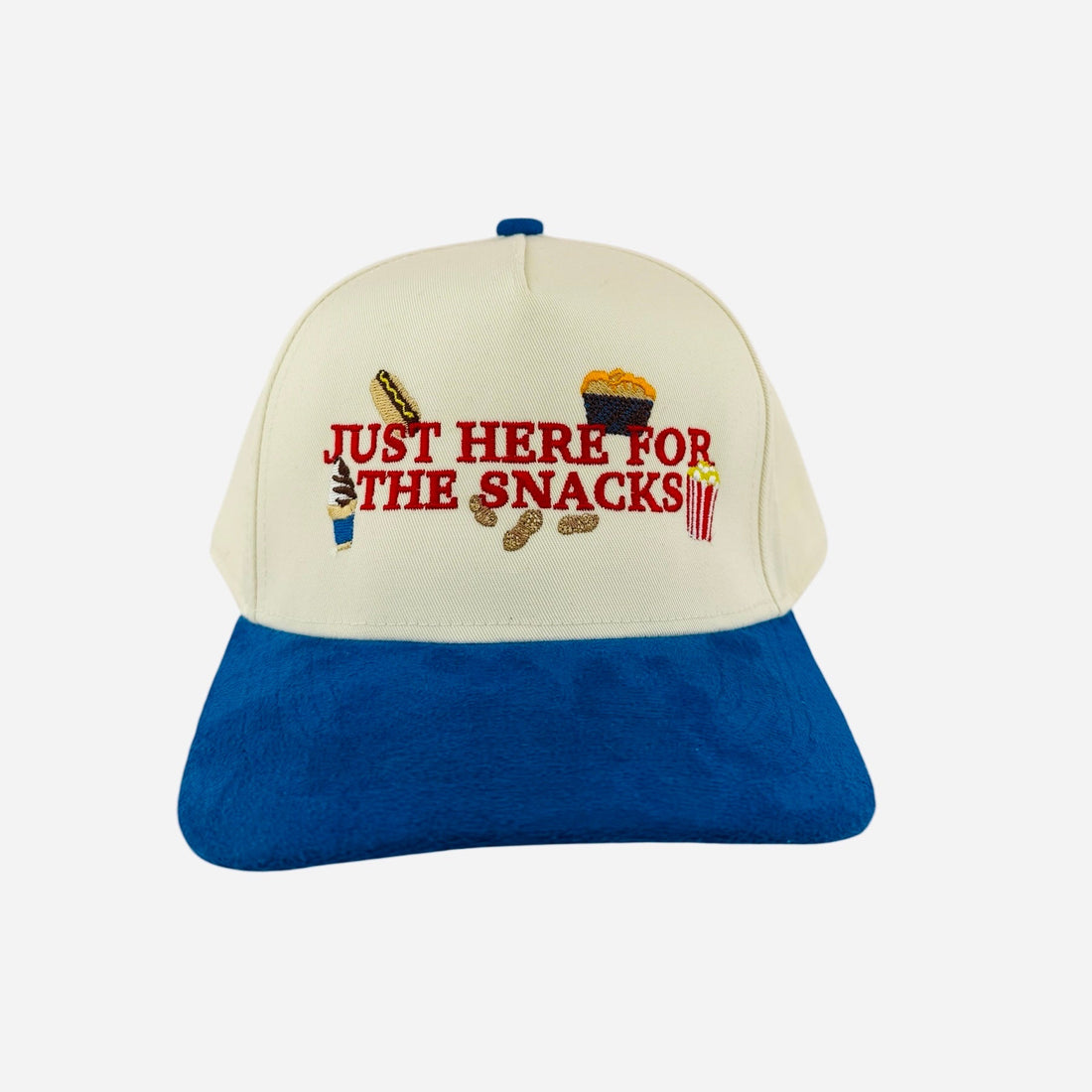 Baseball cap with 'Just Here for the Snacks' text on a table at a baseball stadium.