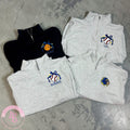 Folded gray and black quarter-zip sweatshirts with embroidered logos on a concrete surface.
