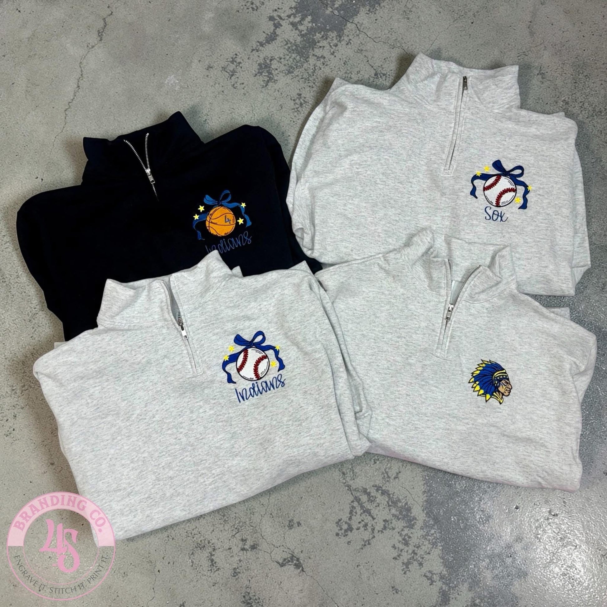 Folded gray and black quarter-zip sweatshirts with embroidered logos on a concrete surface.