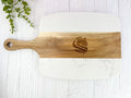 A rectangular wooden serving board with rounded corners, a natural wood handle, and a white marble-look lower section. A dark engraved lion head logo is centered on the wood.