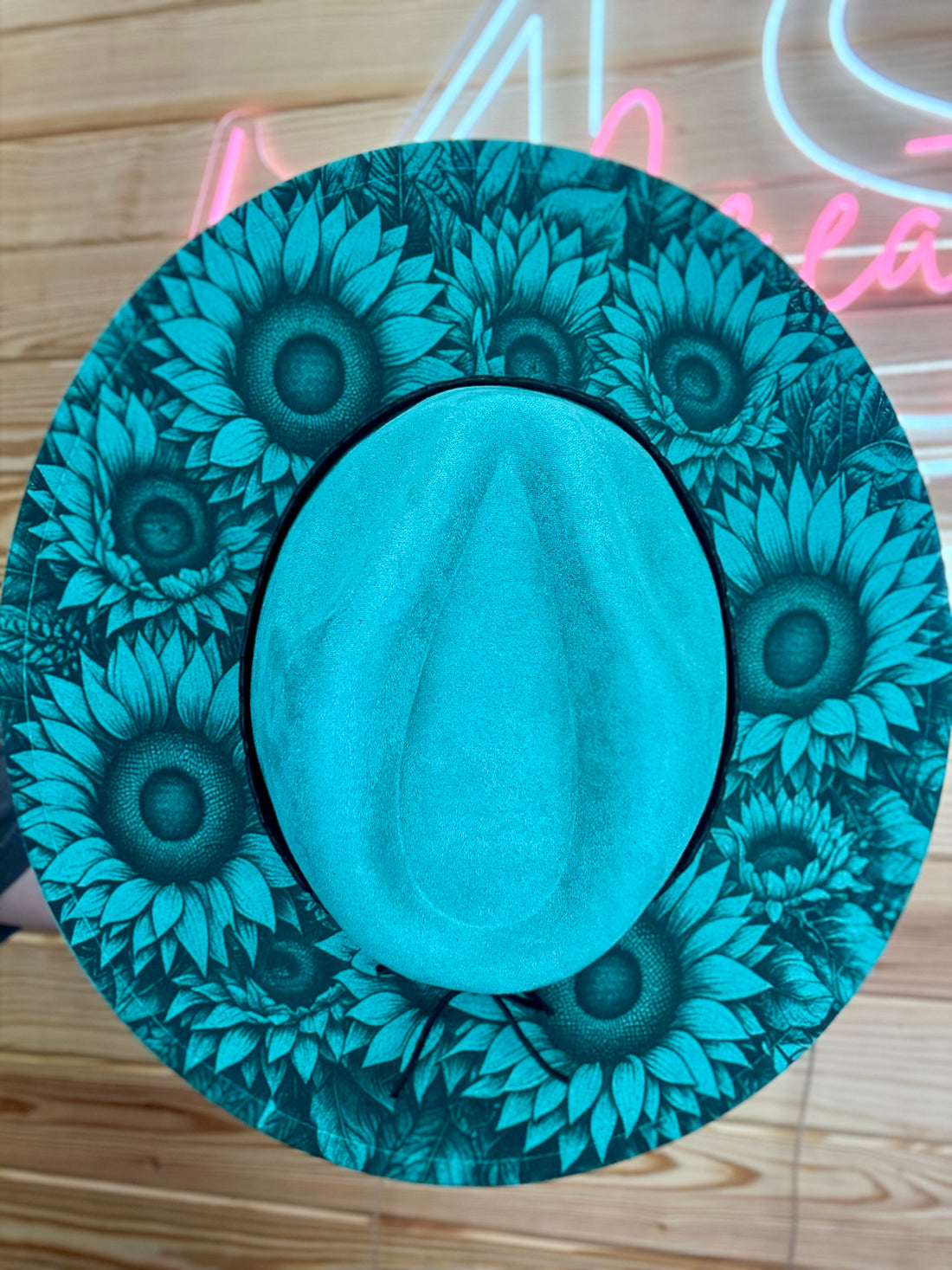 Teal sunflower patterned coaster on a wooden surface with neon sign in the background