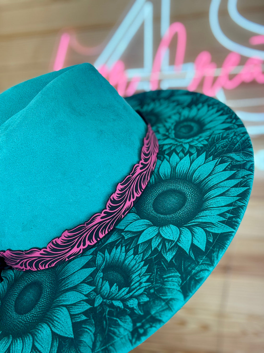 Teal sunflower patterned coaster on a wooden surface with neon sign in the background