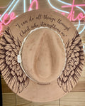 Brown hat with wing designs and text on a wooden surface with neon lights in the background