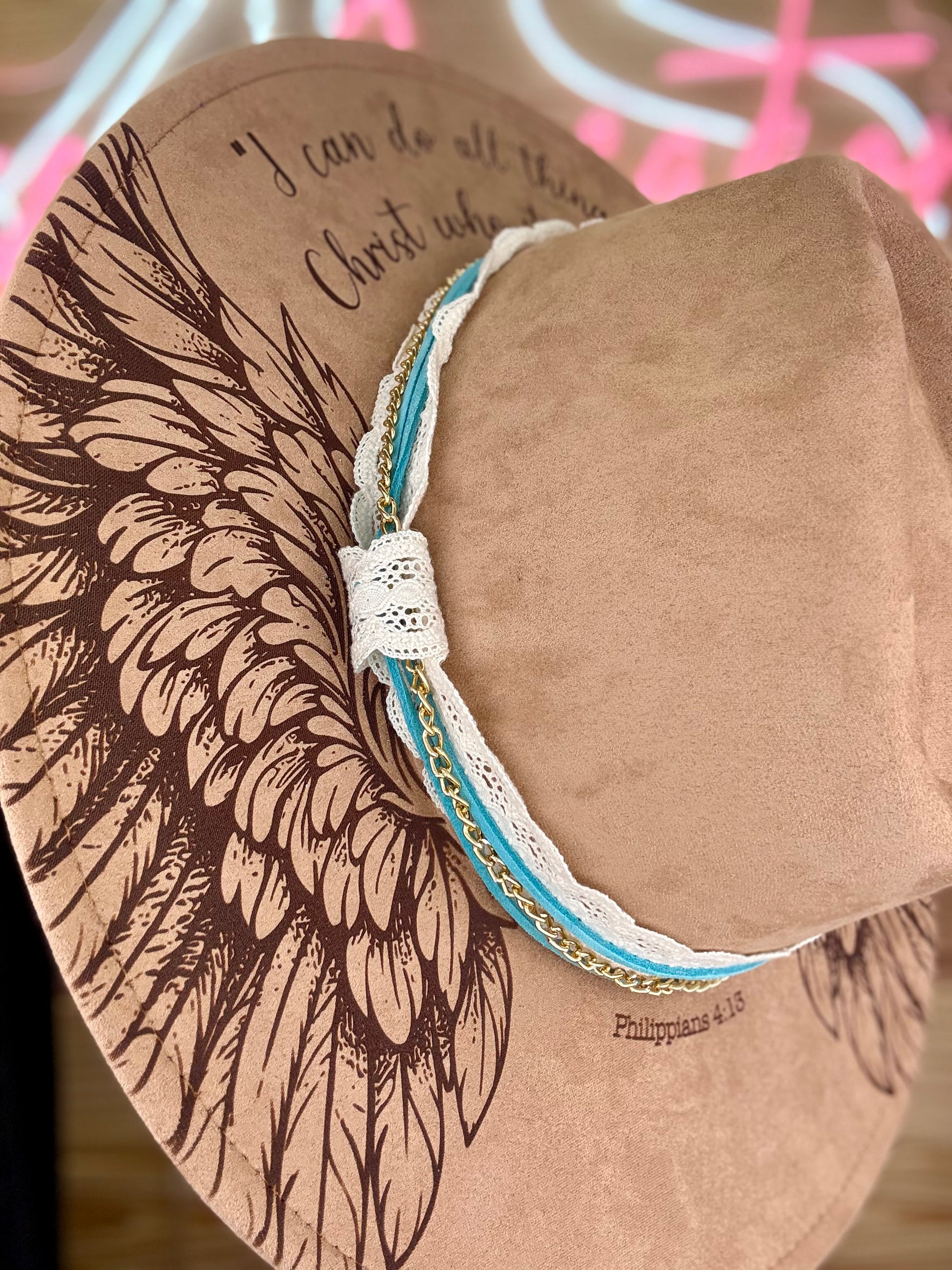 Brown hat with wing designs and a white teal and gold chain hat band