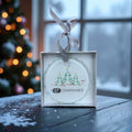 Decorative Christmas ornament with 'DT Companies' logo in a box, blurred Christmas tree in the background
