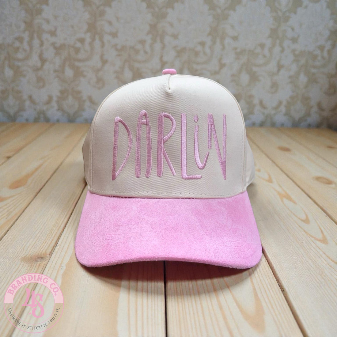 Pink and beige cap with 'Darlin' embroidery on a wooden surface